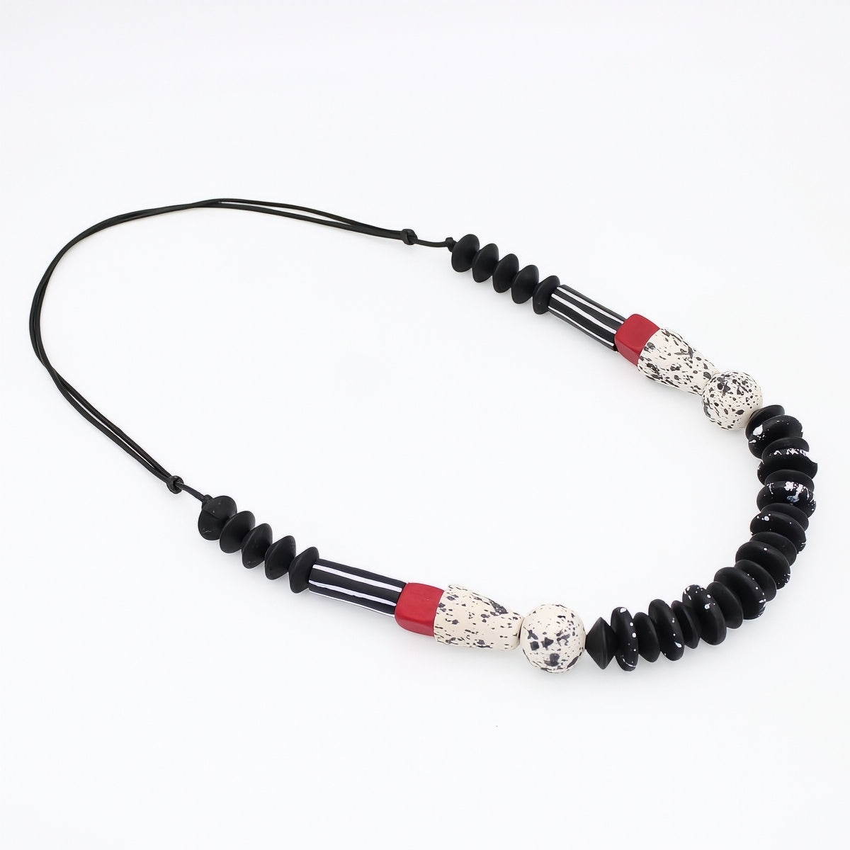 A beaded necklace featuring black disc beads, striped black and white beads, and two red accent beads with white speckled center beads, displayed on a clean white background.
