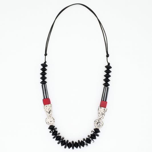 A beaded necklace featuring black faceted beads, black and white striped sections, textured silver-toned details, and small red accent beads, suspended on a black cord against a plain white background.