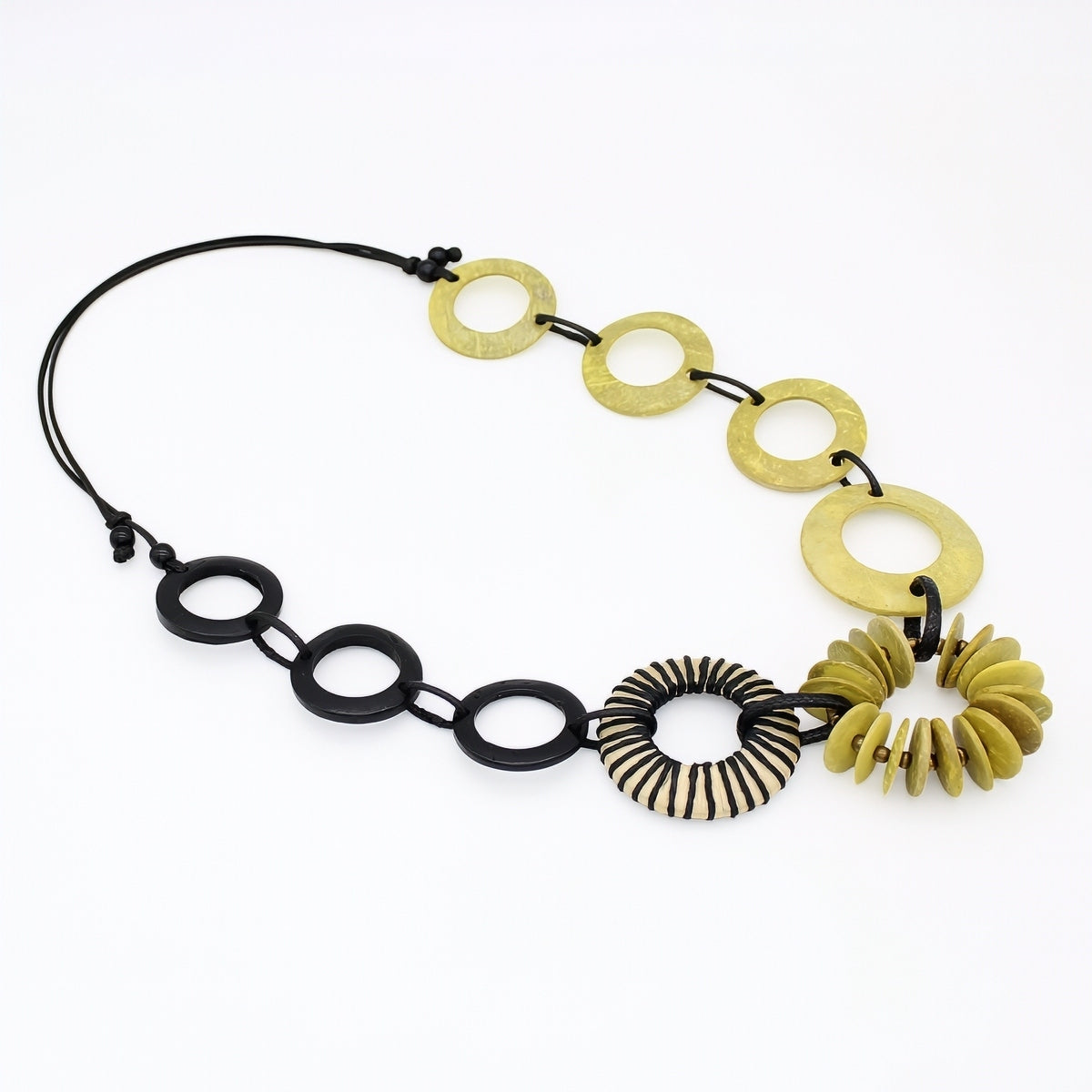 A modern geometric necklace featuring alternating matte black and brushed gold disc links, with one striped black-and-gold ring and a gold petal-like spiral charm, displayed on a clean white background.