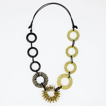 A modern statement necklace featuring alternating matte black circular discs and textured gold-tone disc and sunburst elements, suspended on a black cord against a plain white background.