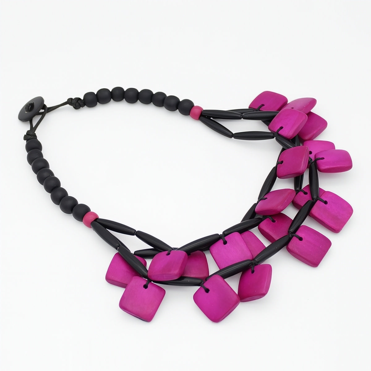 A statement necklace featuring bright magenta-pink square beads and black cylindrical links, displayed on a clean white background.