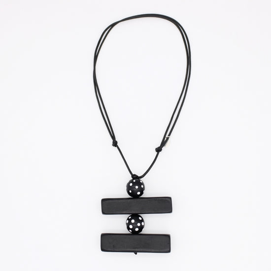 A black geometric pendant necklace featuring two horizontal rectangular bars connected by a central perforated sphere, suspended on a black cord against a plain white background.