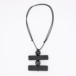 A black geometric pendant necklace featuring two horizontal rectangular bars connected by a central perforated sphere, suspended on a black cord against a plain white background.