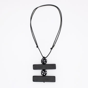 A black geometric pendant necklace featuring two horizontal rectangular bars connected by a central perforated sphere, suspended on a black cord against a plain white background.