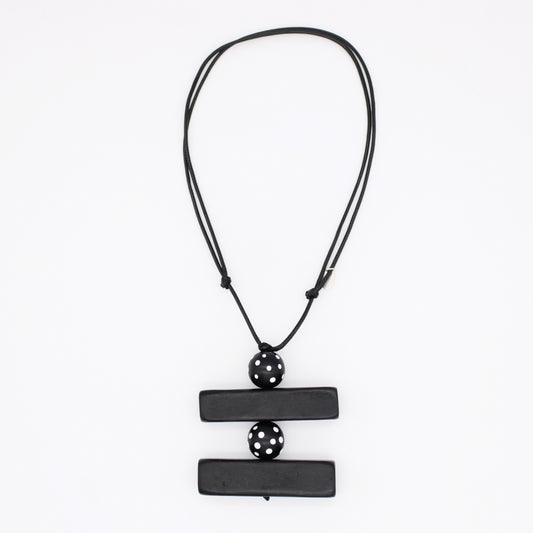 A black geometric pendant necklace featuring two horizontal rectangular bars connected by a central perforated sphere, suspended on a black cord against a plain white background.