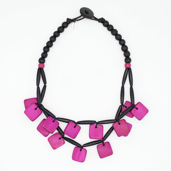 A statement necklace featuring bright magenta-pink square beads and matte black cylindrical beads, arranged in a tiered bib style on a plain white background.