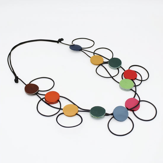 A multi-colored wooden disc necklace with black elastic loops, displayed on a clean white background.