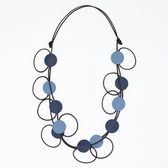 A modern multi-strand necklace featuring matte circular discs in navy and light blue, suspended on a black cord against a plain white background.