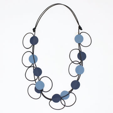A modern multi-strand necklace featuring matte circular discs in navy and light blue, suspended on a black cord against a plain white background.