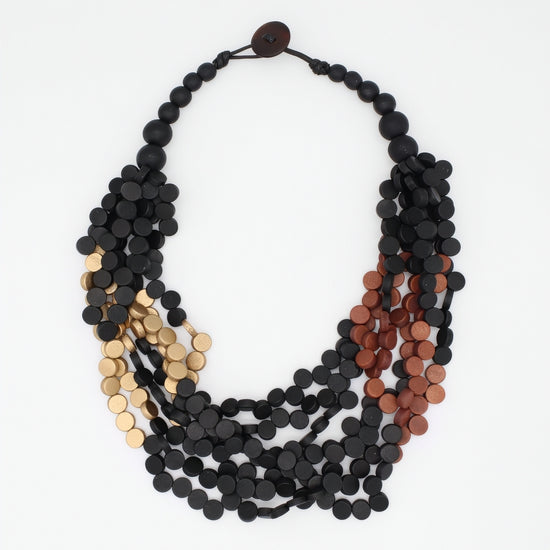 A multi-strand statement necklace featuring matte black, metallic gold, and metallic copper disc beads, arranged in a layered circular style on a plain white background.
