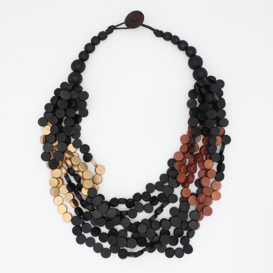 A multi-strand statement necklace featuring matte black, metallic gold, and metallic copper disc beads, arranged in a layered circular style on a plain white background.