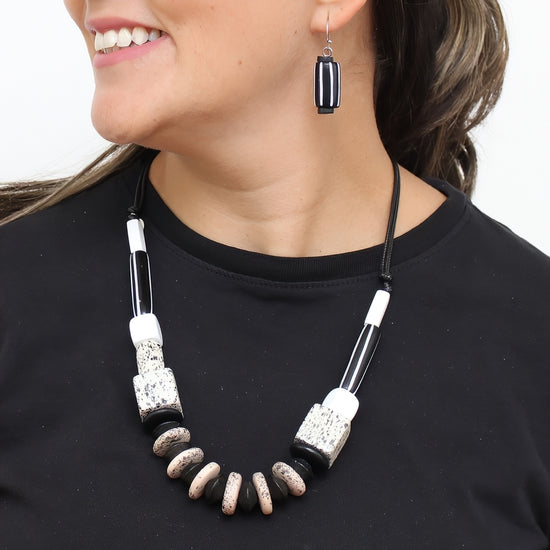A close-up of a woman wearing a black and white beaded necklace with polished stone-like beads and a matching black earring against a plain white background.