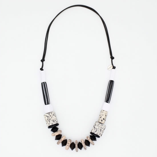A statement necklace featuring a black cord, white cylindrical beads, black striped beads, and textured black and beige geometric beads, displayed on a clean white background.