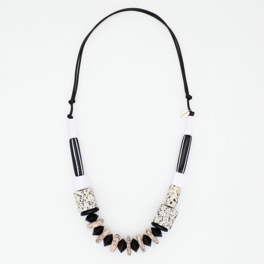 A statement necklace featuring a black cord, white cylindrical beads, black striped beads, and textured black and beige geometric beads, displayed on a clean white background.