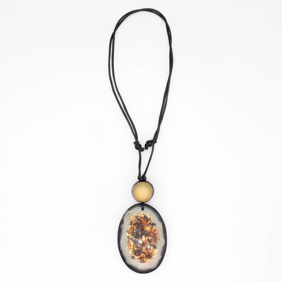 A black cord necklace featuring a large oval pendant with a dried floral or botanical inlay, accented by a small round gold bead above it, shown against a plain white background.