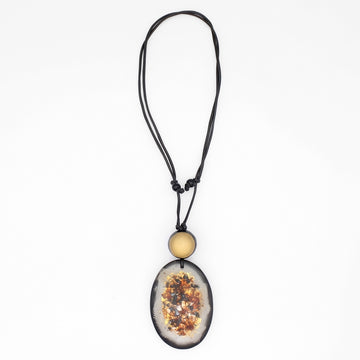 A black cord necklace featuring a large oval pendant with a dried floral or botanical inlay, accented by a small round gold bead above it, shown against a plain white background.