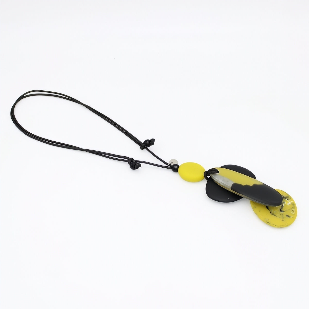 A modern pendant necklace featuring a black cord, a small yellow disc bead, and a larger marbled black and yellow pendant on a white background.