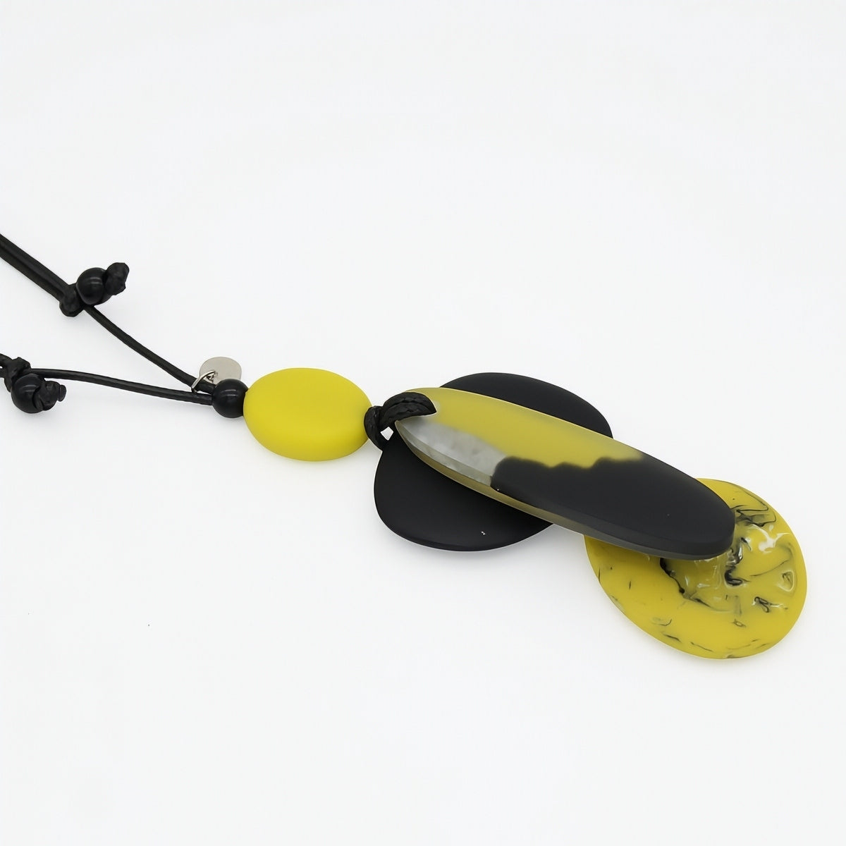 A modern pendant necklace featuring a black cord, a small yellow bead, and a large central pendant with a black and yellow marbled design, flanked by two flat yellow disc pendants on a white background.