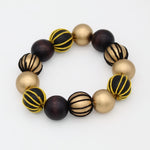 A beaded stretch bracelet featuring alternating matte gold, glossy dark brown, and striped black-and-gold beads, displayed on a clean white background.