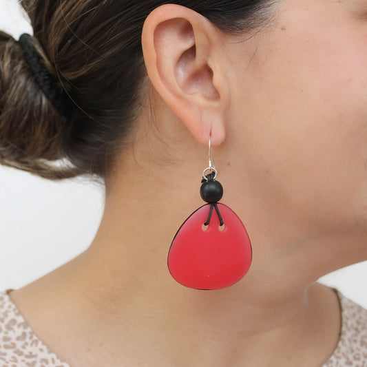 A close-up of a person's ear wearing a dangling earring with a bright red teardrop-shaped drop and a small black bead accent.