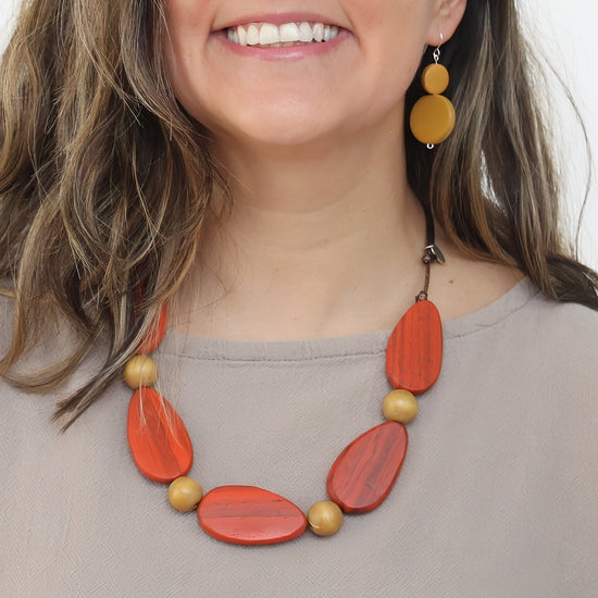 Woman wearing a orange and gold necklace with matching earrings on a plain background