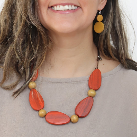 Woman wearing a orange and gold necklace with matching earrings on a plain background