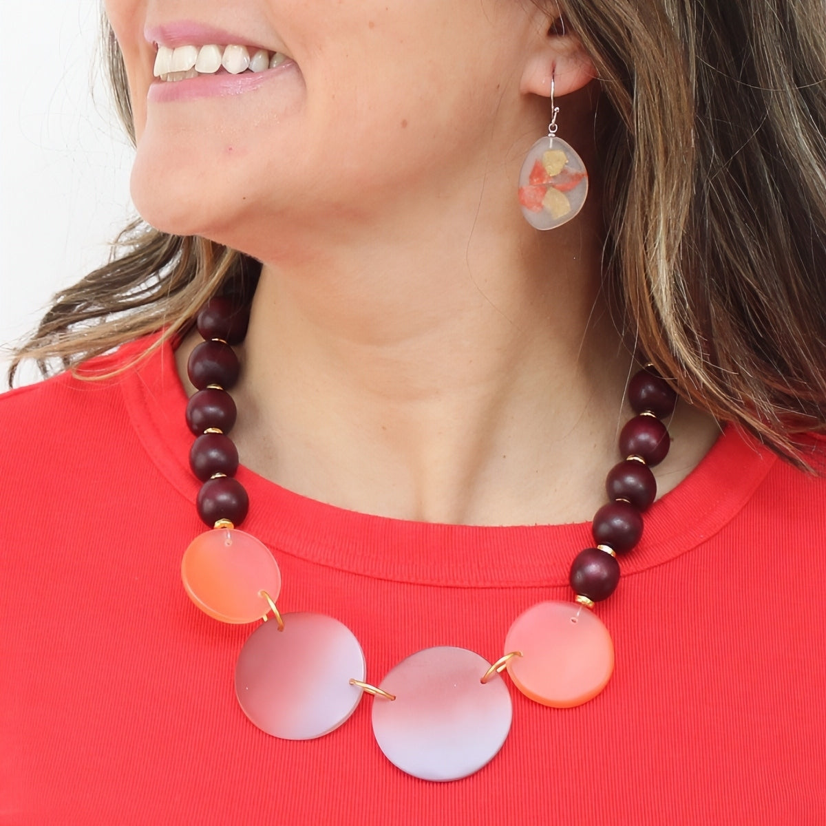 Woman wearing a colorful necklace with pink and purple circular beads on a red shirt.