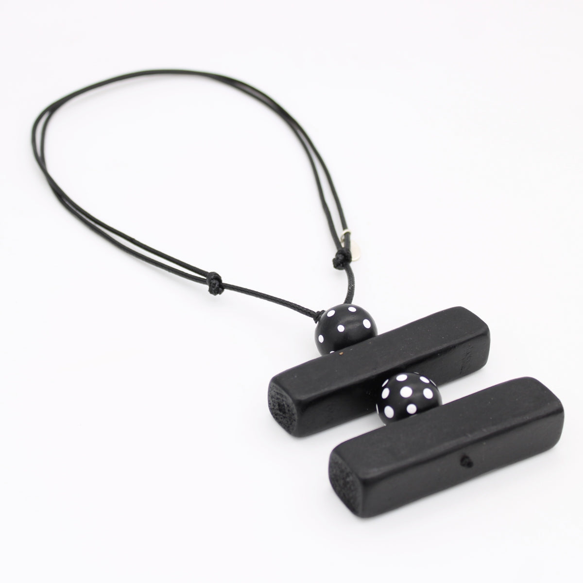Black wooden pendant necklace with two rectangular bars connected by a black cord and accented with two black beads featuring white polka dots, shown on a plain white background.